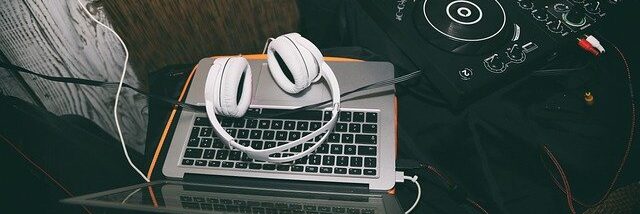 The image shows a DJ setup. There is a laptop with a pair of white headphones resting on its keyboard.